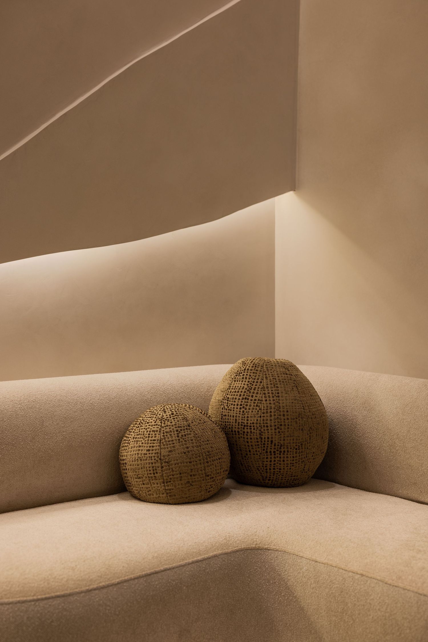 Two textured woven sphere decorative pillows on a curved beige velvet sofa with soft lighting.