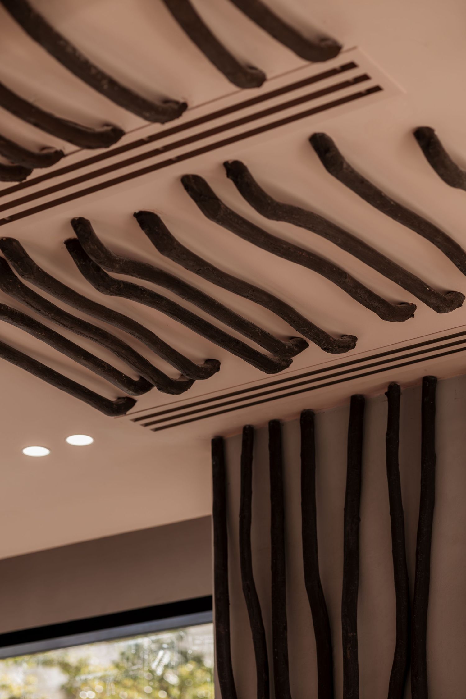 Decorative ceiling detail with organic dark brown wavy branch-like sculptures on a beige surface with curtains below.