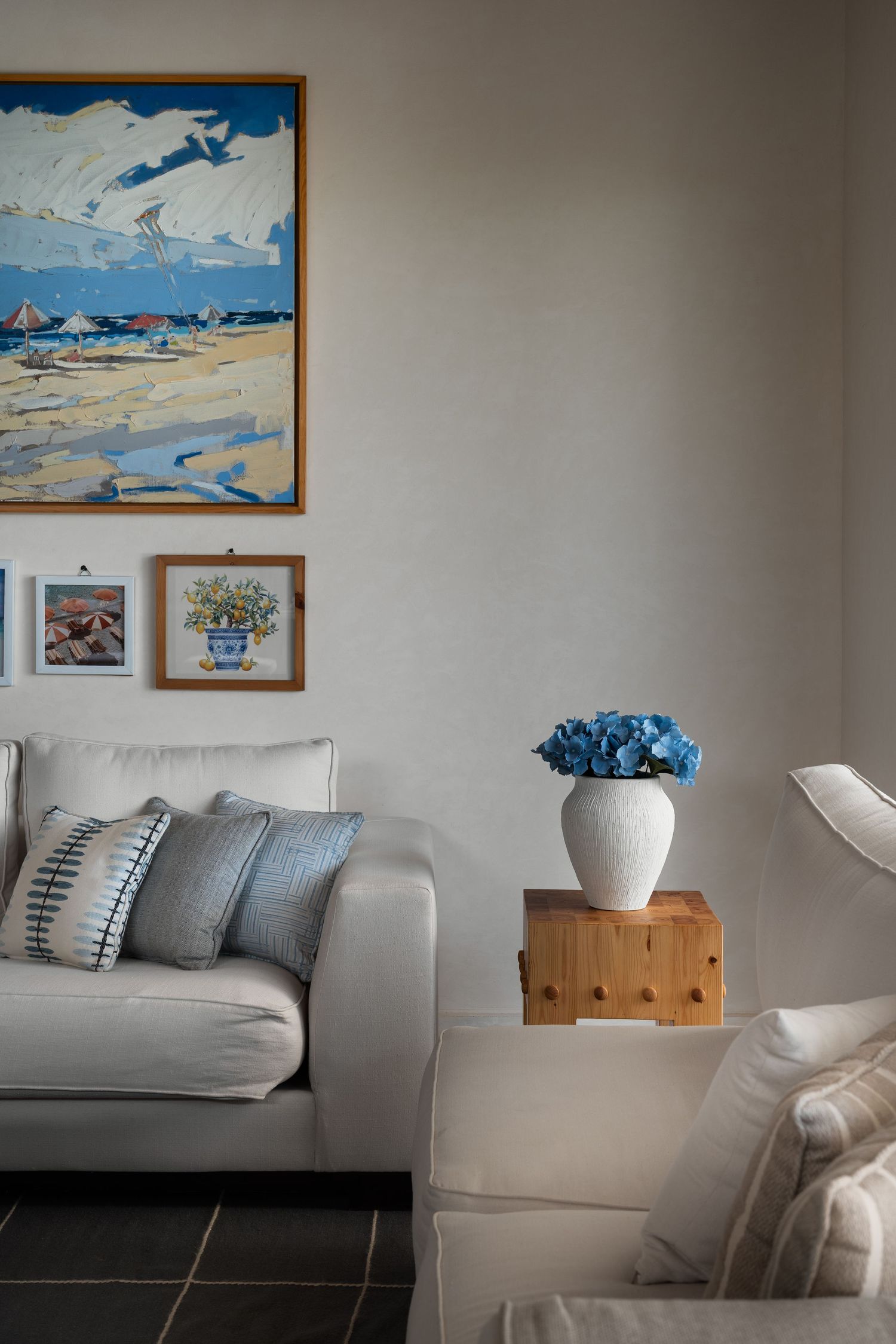 Coastal living room with white sofa, blue hydrangeas, and nautical artwork on neutral walls.