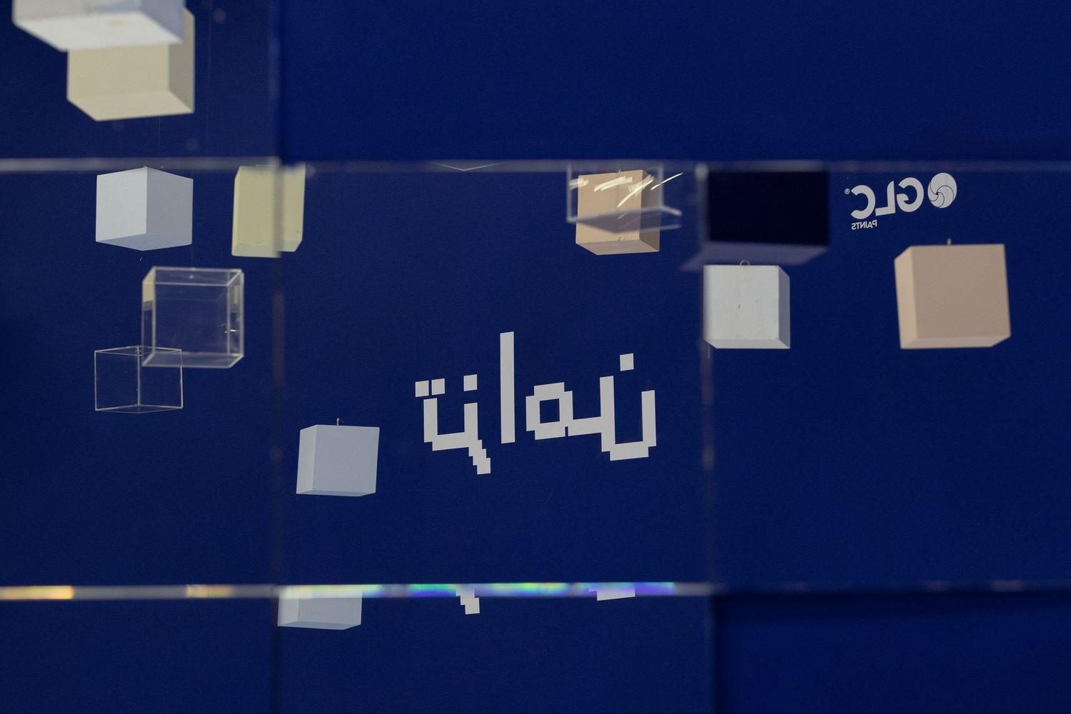 Blue display panel featuring Arabic calligraphy text with decorative floating cube graphics and a logo.