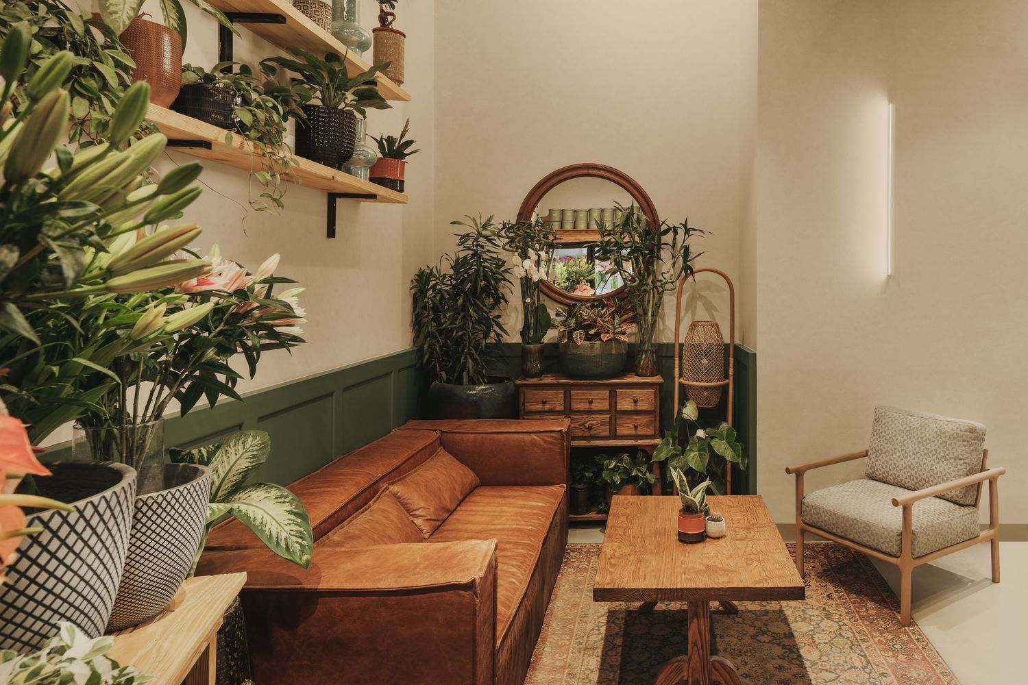 Bohemian living room with brown leather sofa, lush indoor plants, wooden shelves, and round mirror above vintage dresser.