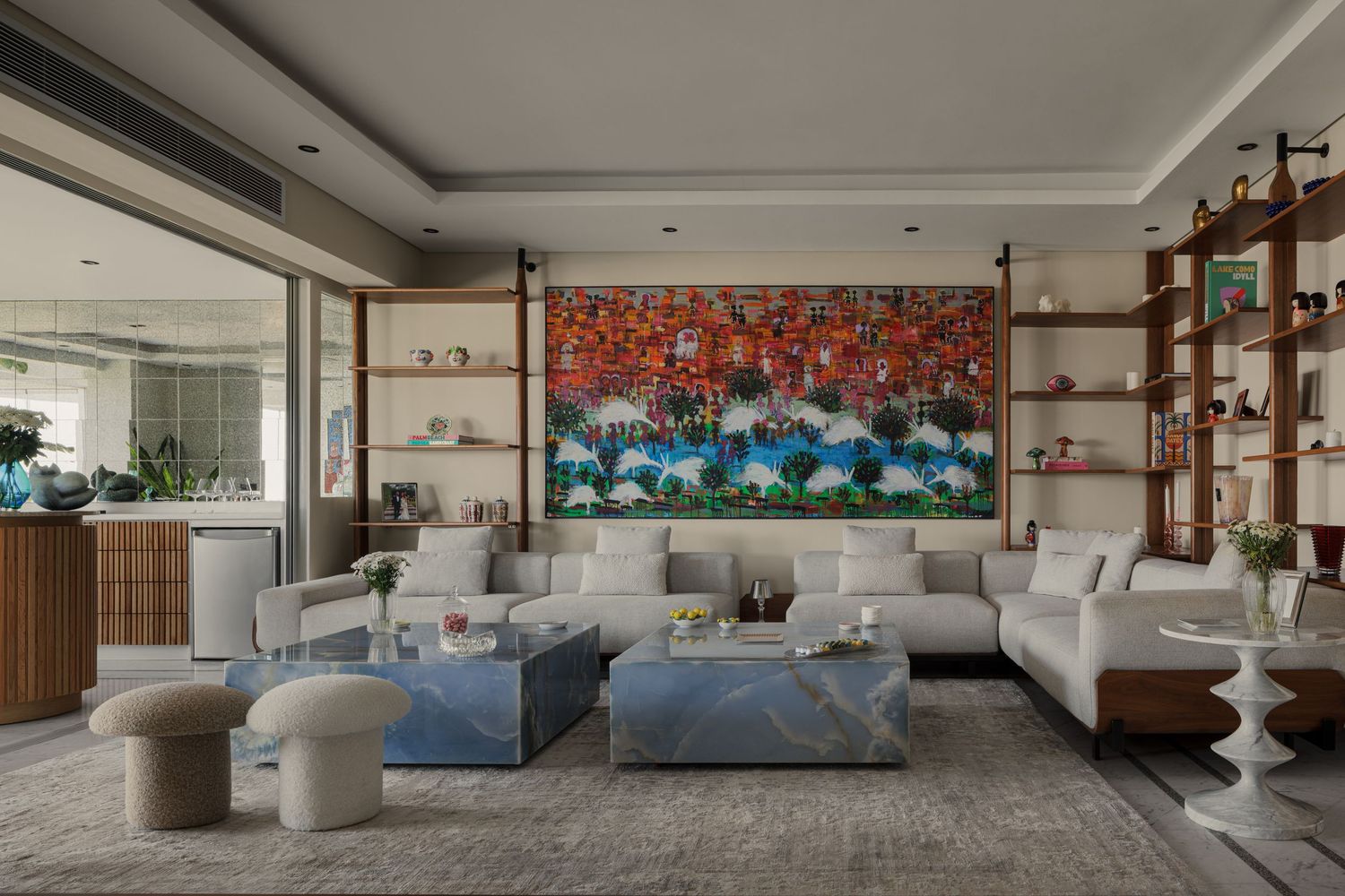 Luxury living room with large colorful abstract artwork, white sectional sofa, blue marble coffee tables, and wooden shelving.