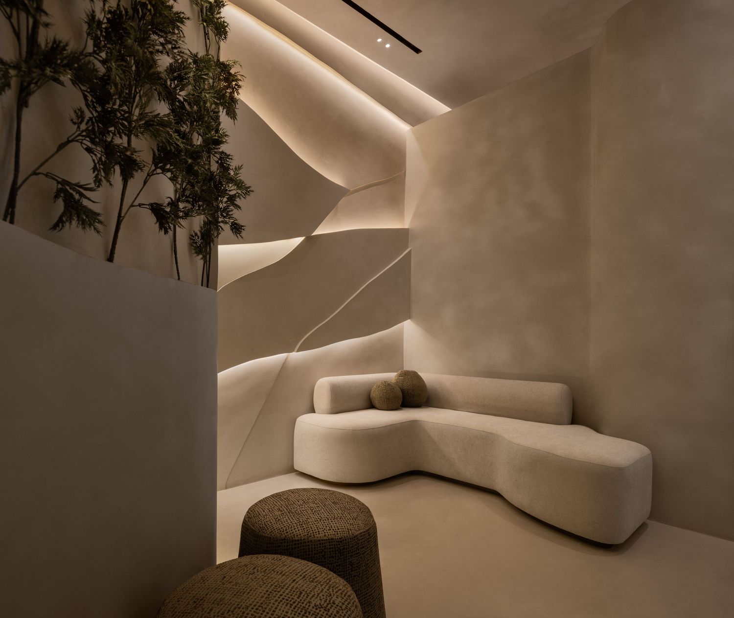 Modern minimalist lounge with curved white bouclé sofa, woven stools, and sculptural staircase with ambient lighting.