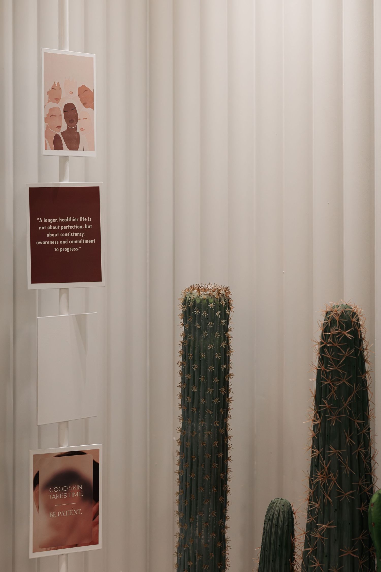 Close-up of tall green cacti against white ribbed wall panels with motivational health quote cards displayed nearby.