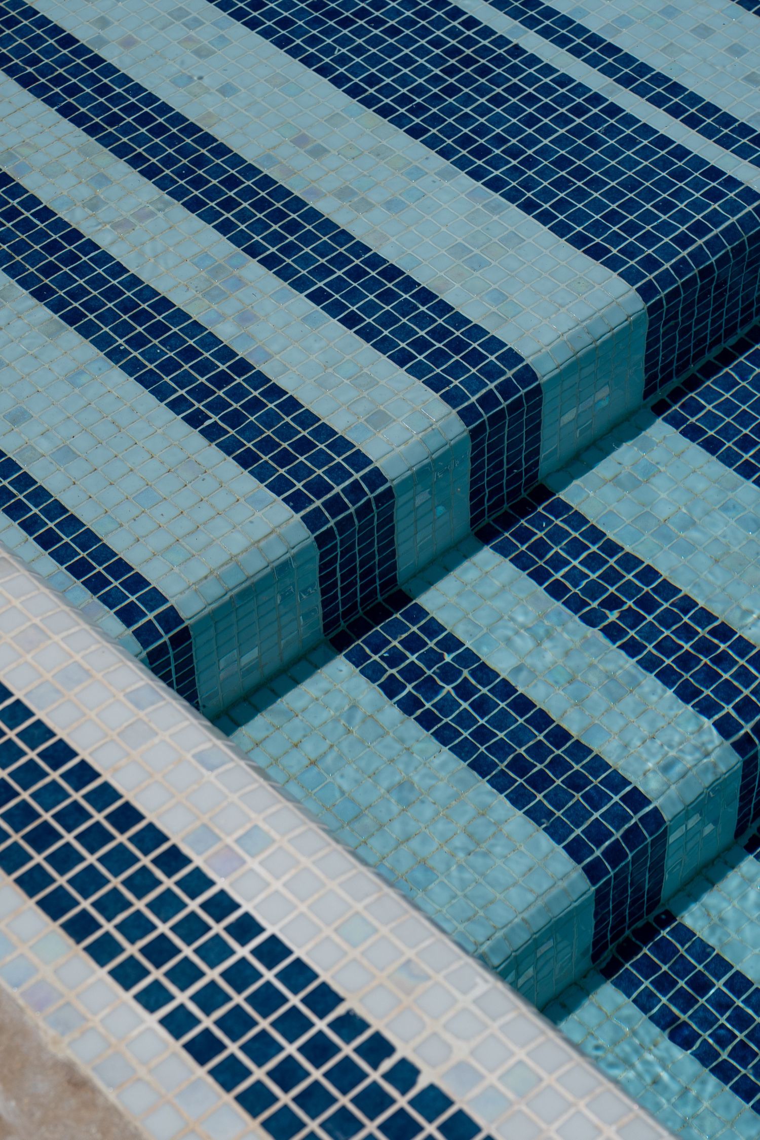 Close-up of blue and teal mosaic tile pool steps submerged in clear water.