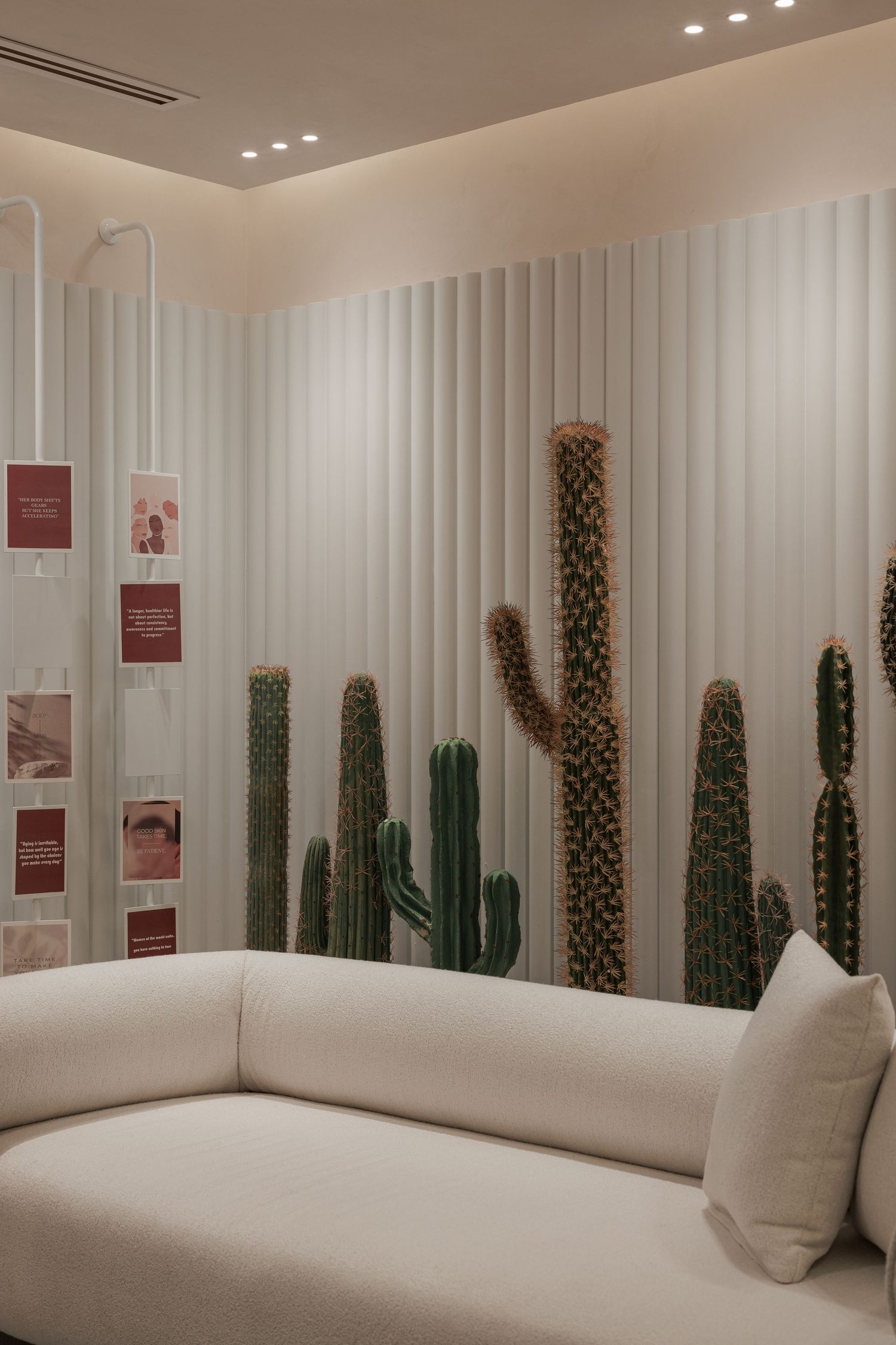 Serene beauty lounge with large cactus wall mural, white textured sofa, fluted panels, and warm recessed ceiling lights.