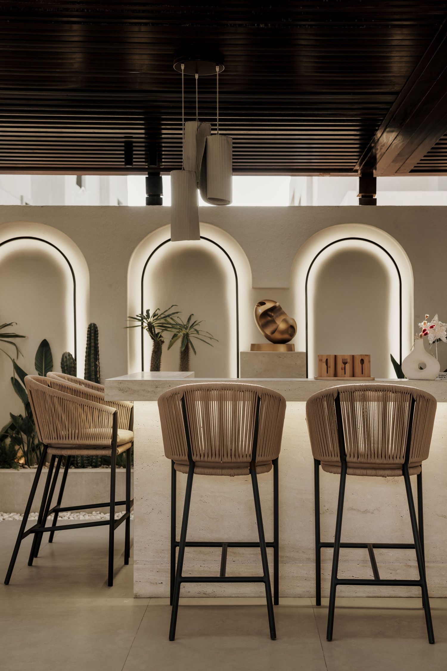Elegant bar seating with woven rattan stools at a marble counter, framed by illuminated arched wall niches.