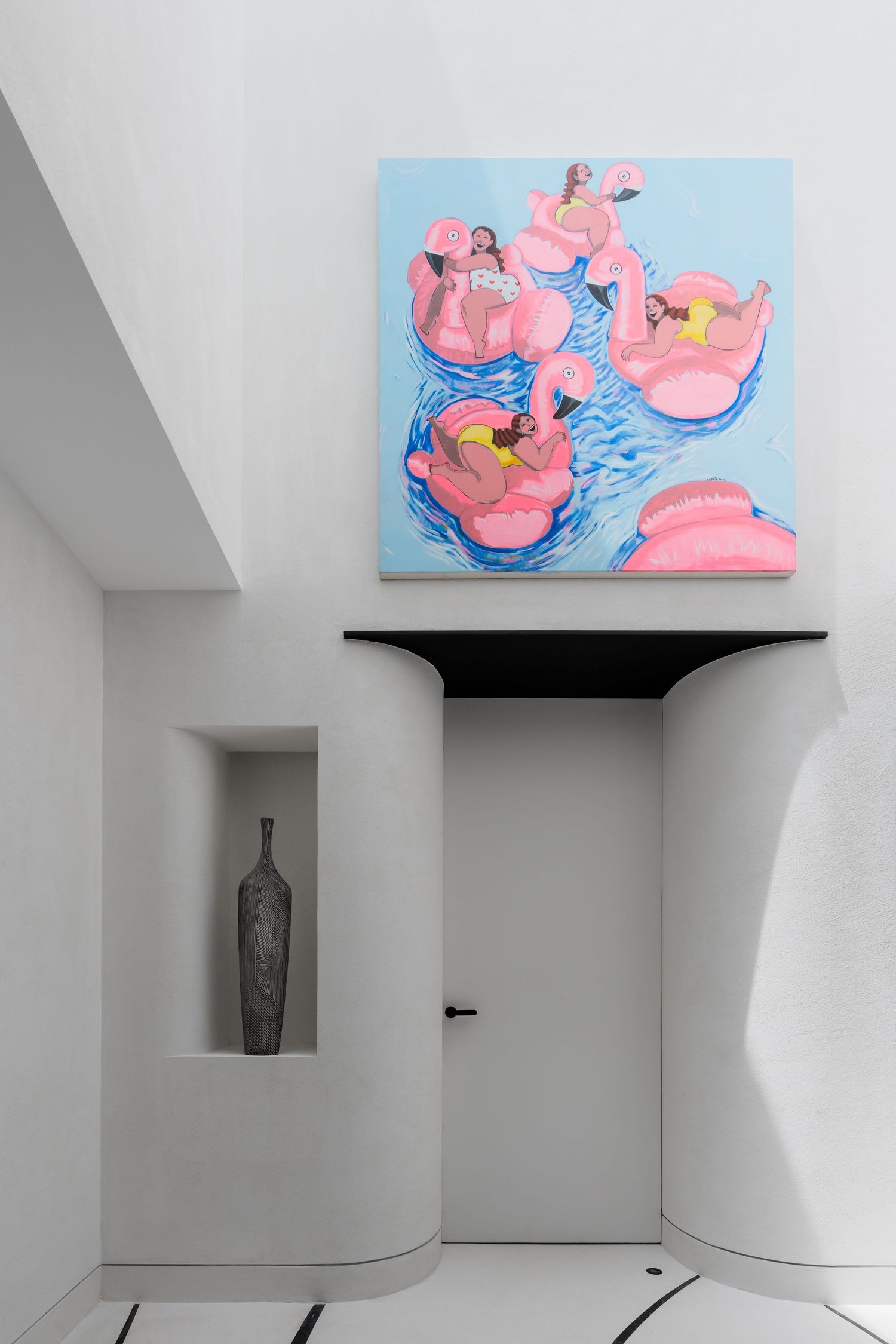 Contemporary white hallway featuring vibrant pink flamingo float painting above minimalist black shelf.
