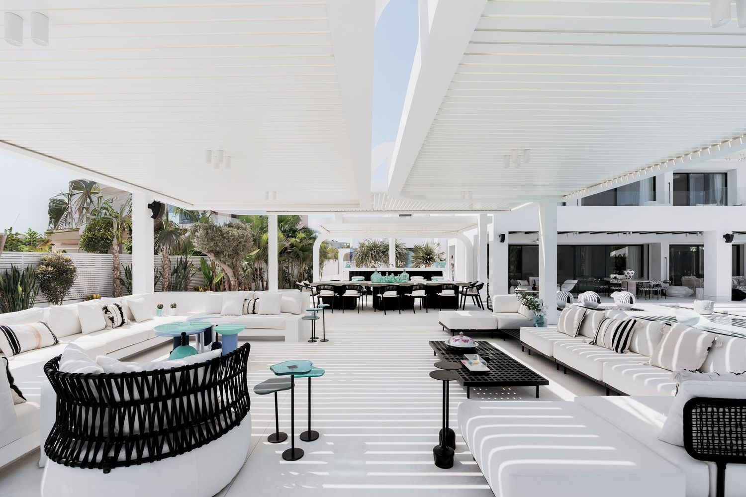 Luxurious white outdoor patio with modern furniture, striped flooring, and open pergola roof in an elegant resort setting.