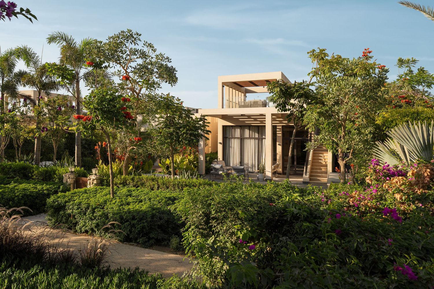 Luxurious contemporary villa nestled among vibrant tropical gardens with bougainvillea and palm trees at sunset.