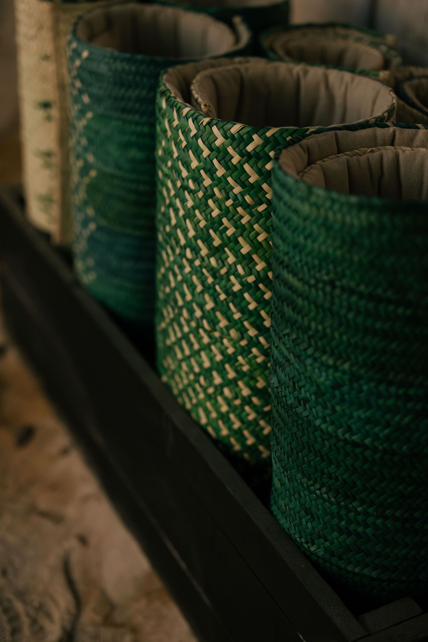 Close-up of green and beige woven wicker baskets with fabric lining arranged in a dark wooden tray.