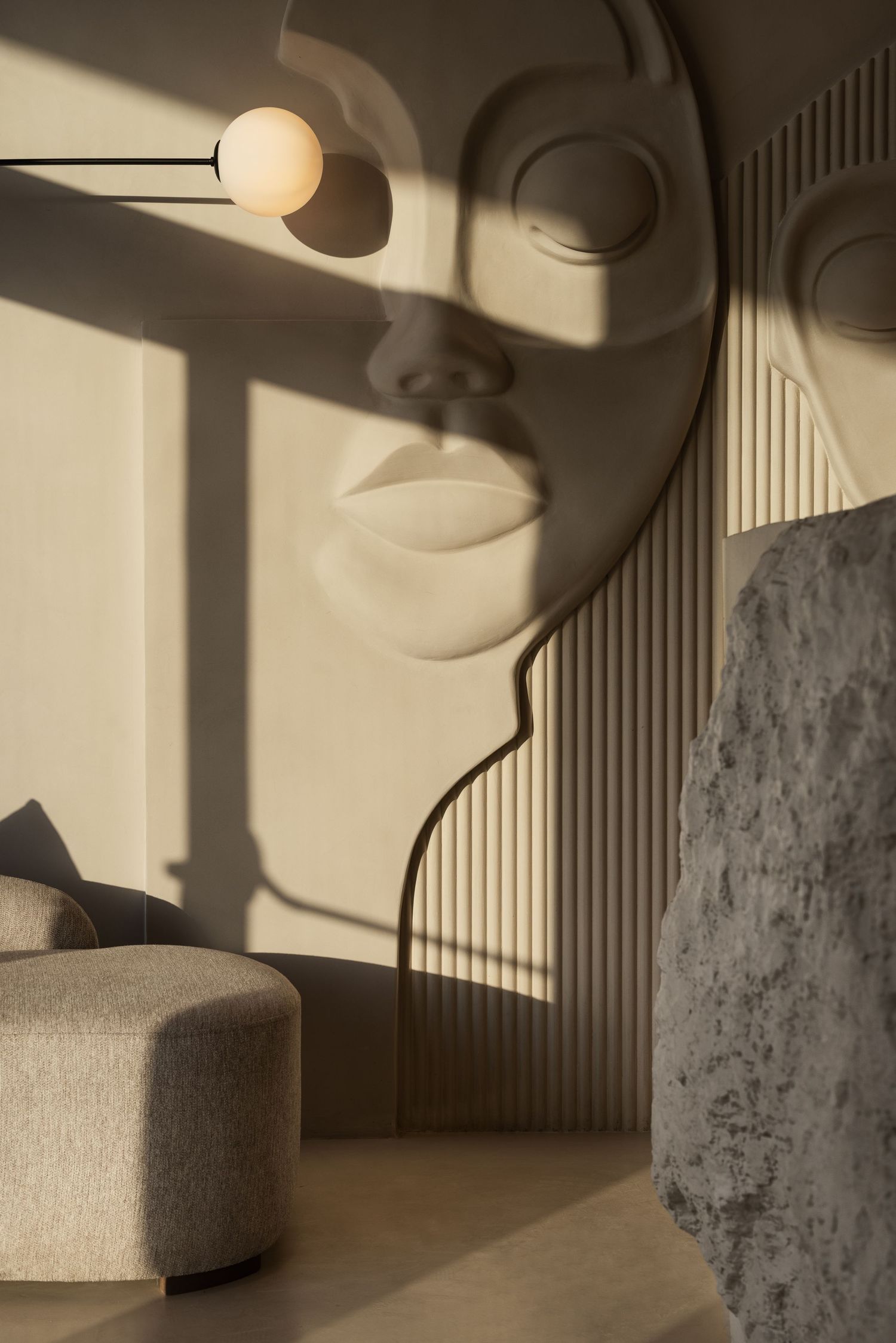 Sculptural face wall art with beige tones, globe pendant lamp, textured stone, and curved floor lamp in modern interior.