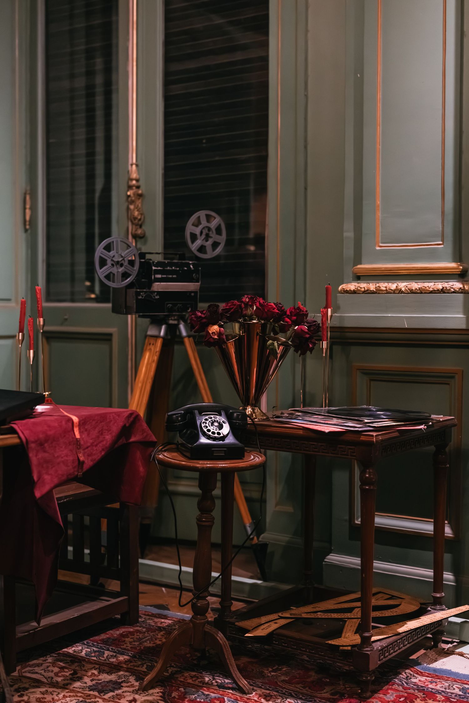 Vintage room interior with a rotary phone, film projector on tripod, and red roses on antique furniture.