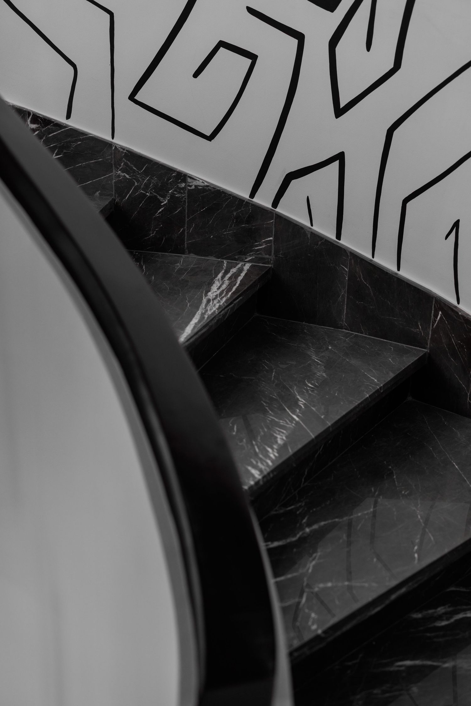Close-up black and white view of dark marble spiral staircase steps with bold geometric patterned wall mural.
