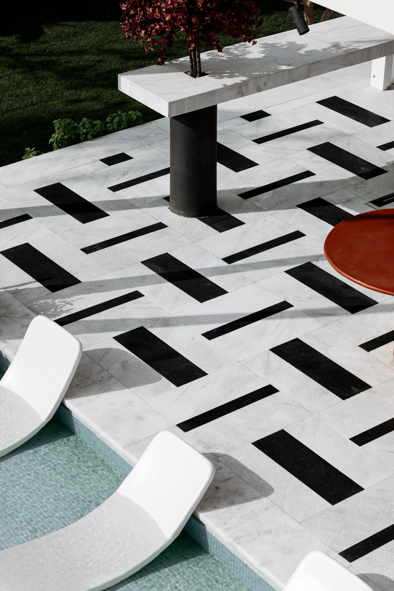 Overhead view of black and white geometric marble tiles with white sun loungers by pool.