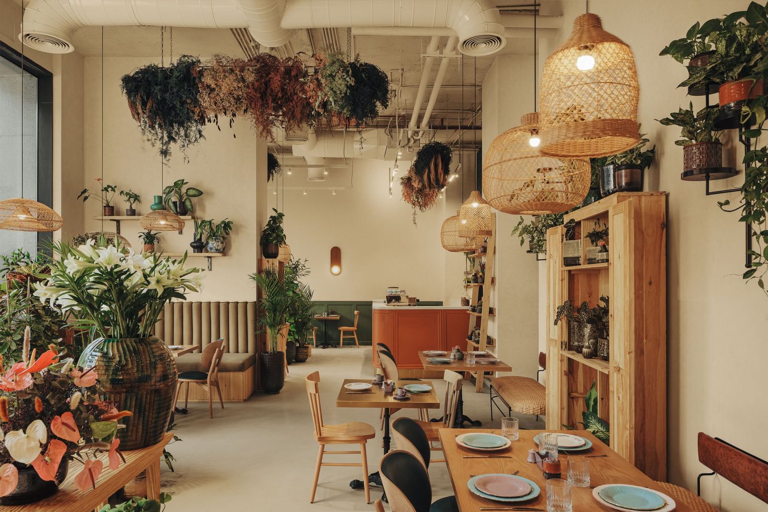 Bright bohemian restaurant interior with dried flower ceiling installations, rattan pendant lights, and lush greenery.