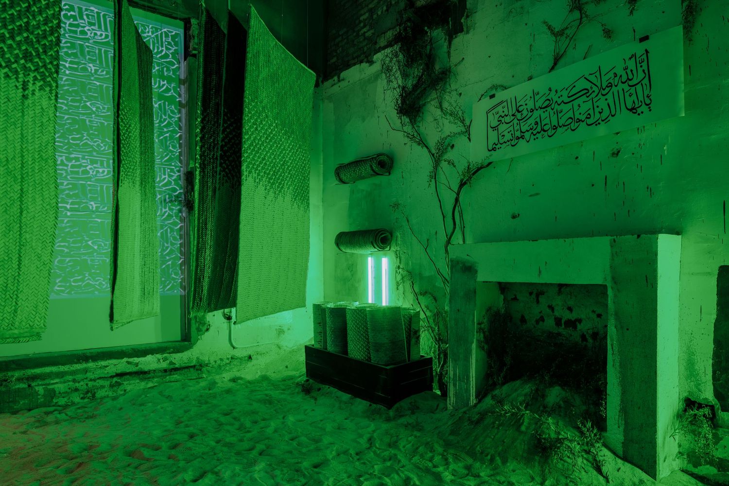 Eerie green-lit abandoned room with Arabic calligraphy textiles, deteriorating walls, and a concrete fireplace.