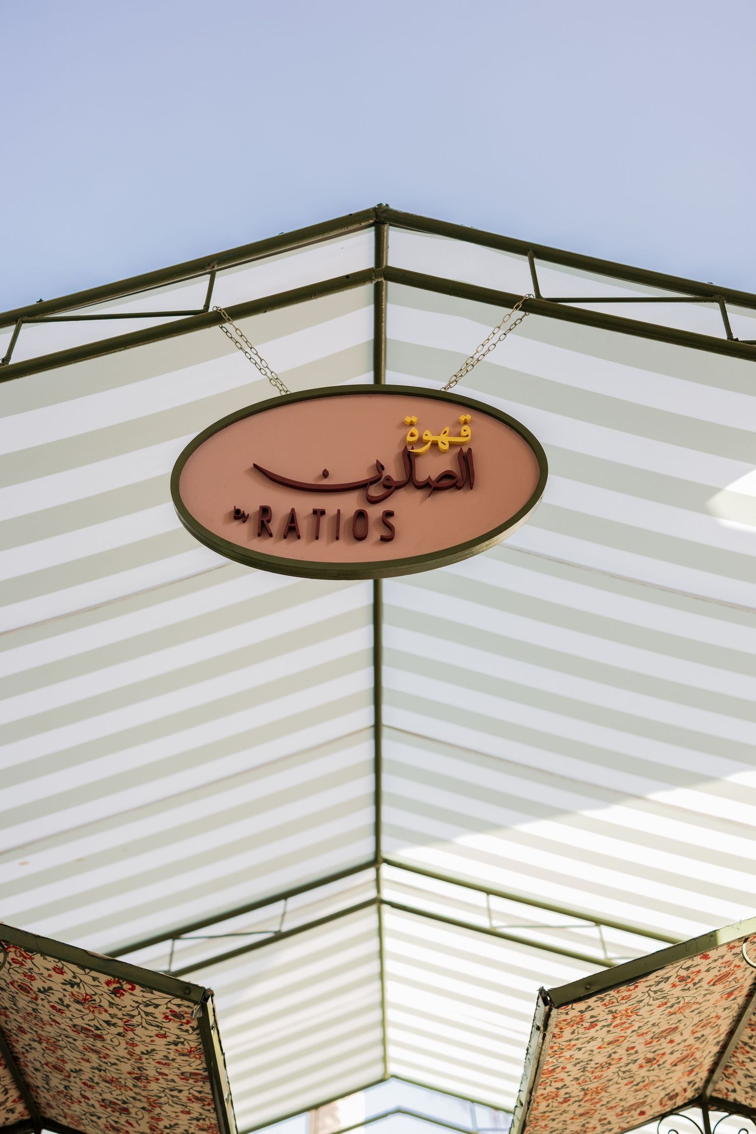 Decorative striped canopy ceiling with oval sign reading Ratios in Arabic and English lettering.