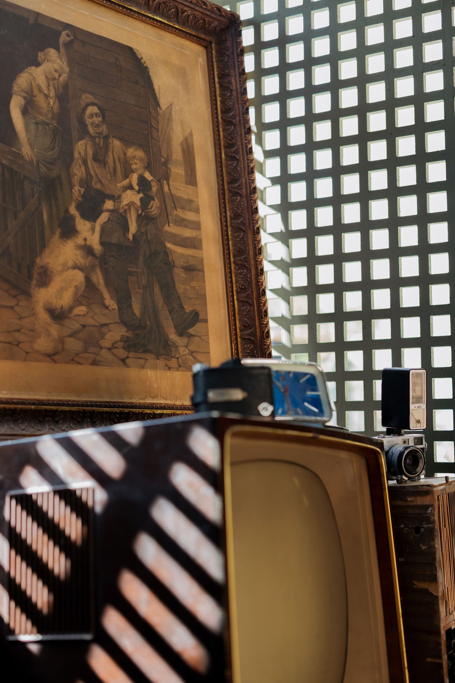 Vintage framed portrait painting above retro television set with old camera near latticed window.