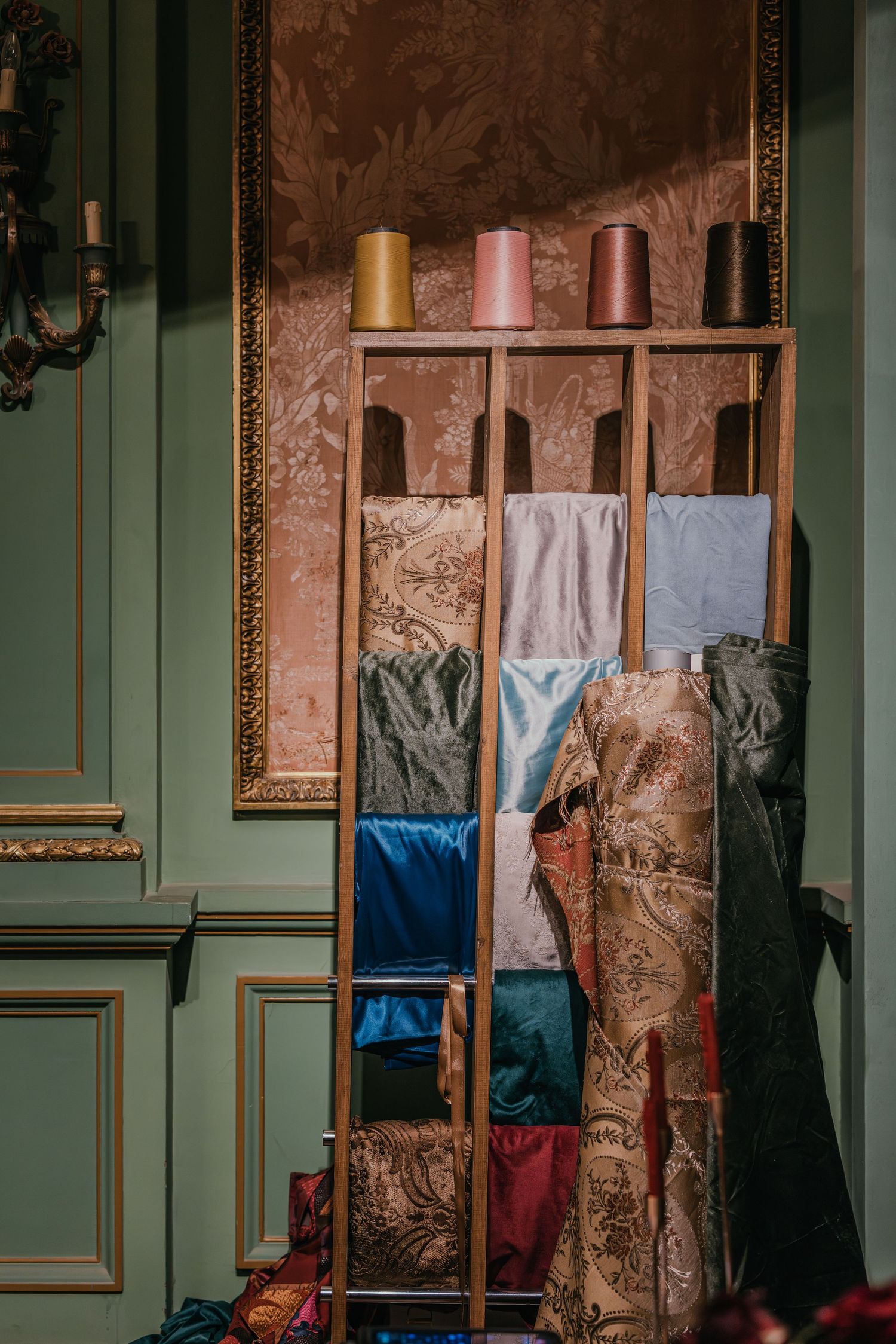 Wooden shelving unit displaying colorful silk fabrics and thread spools in an elegant room.