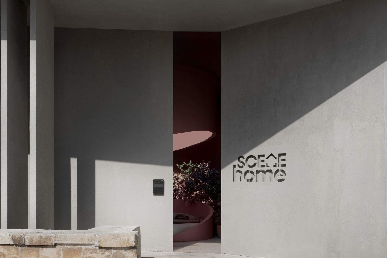 Minimalist exterior entrance of SOECE Home store with grey concrete walls and a glimpse of burgundy interior.