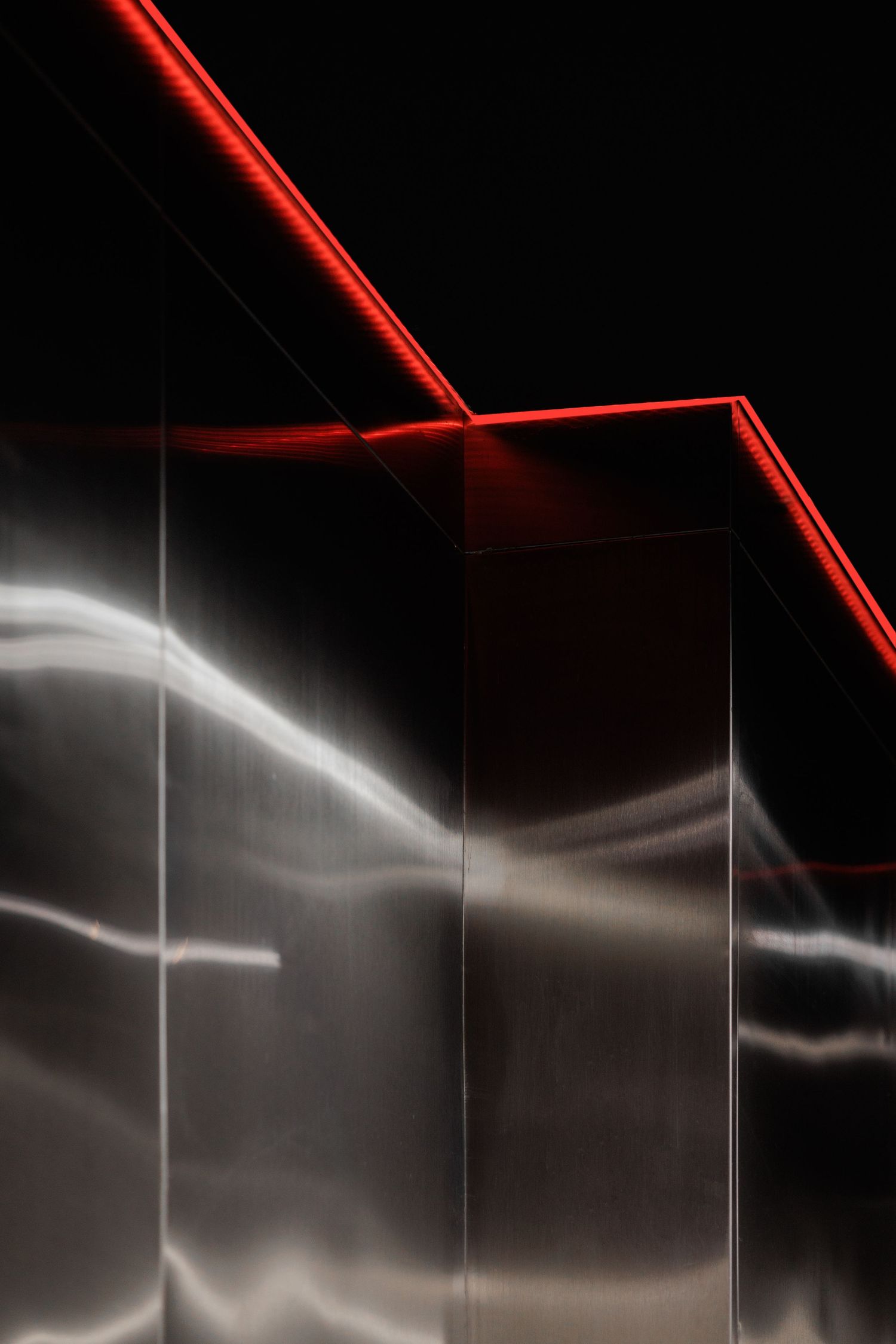 Abstract red neon lights reflecting on metallic walls in dark architectural interior.