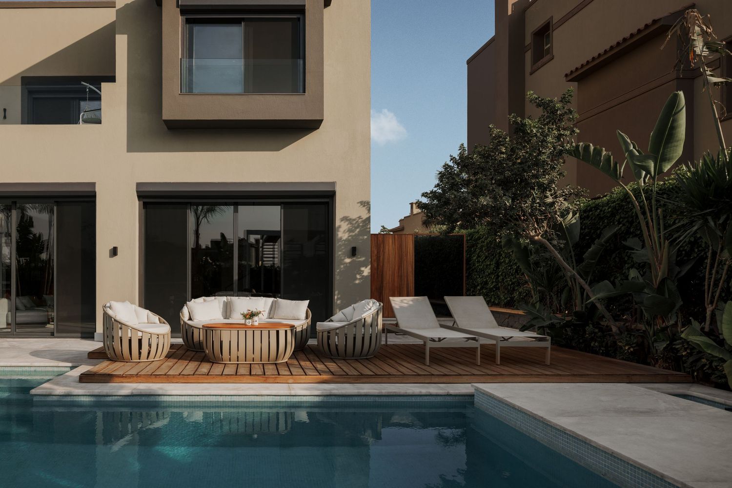 Modern villa exterior with private pool, outdoor lounge furniture, and lush tropical landscaping.