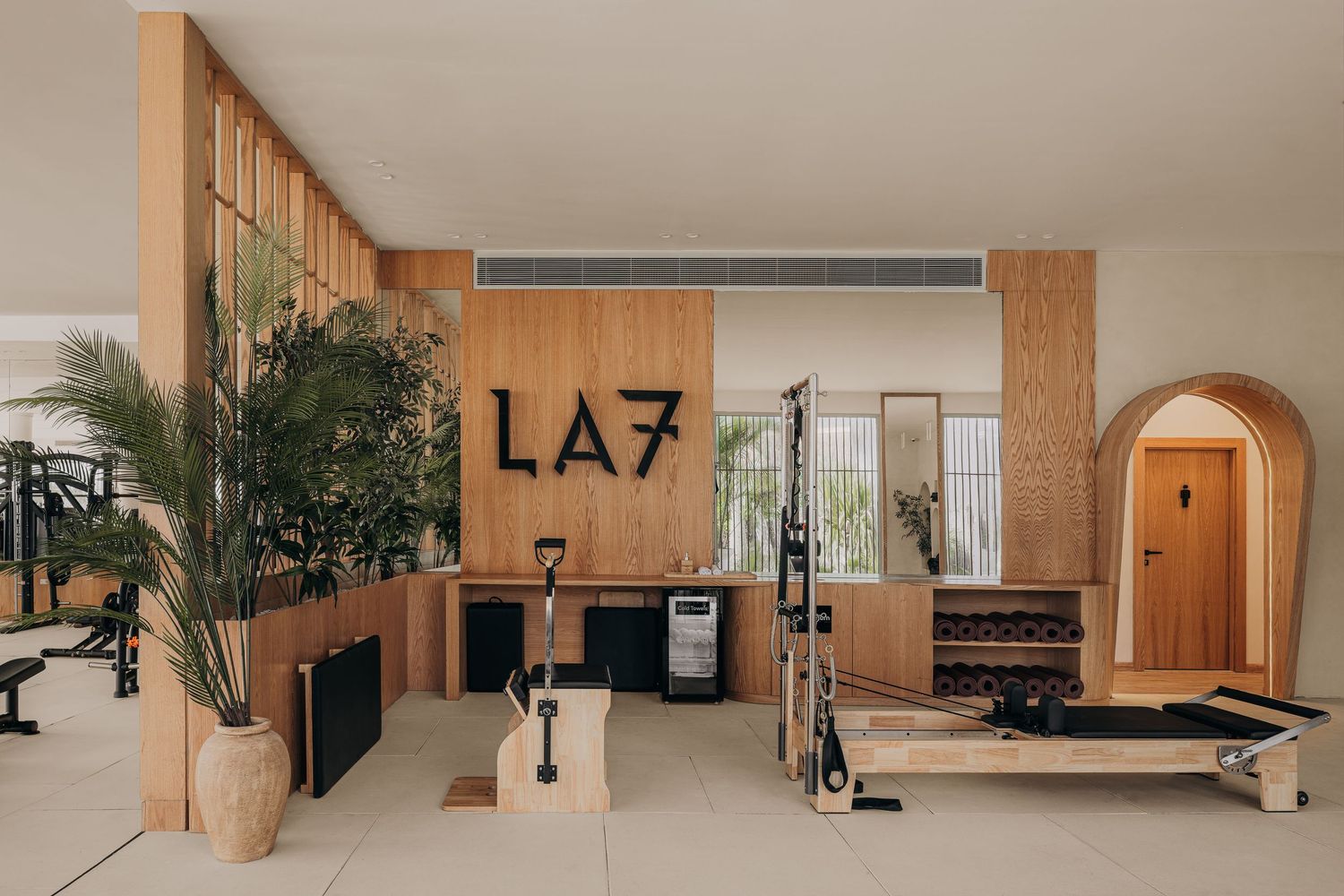 Modern LA7 fitness studio with pilates reformer, wooden accents, and lush indoor plants in a minimalist space.