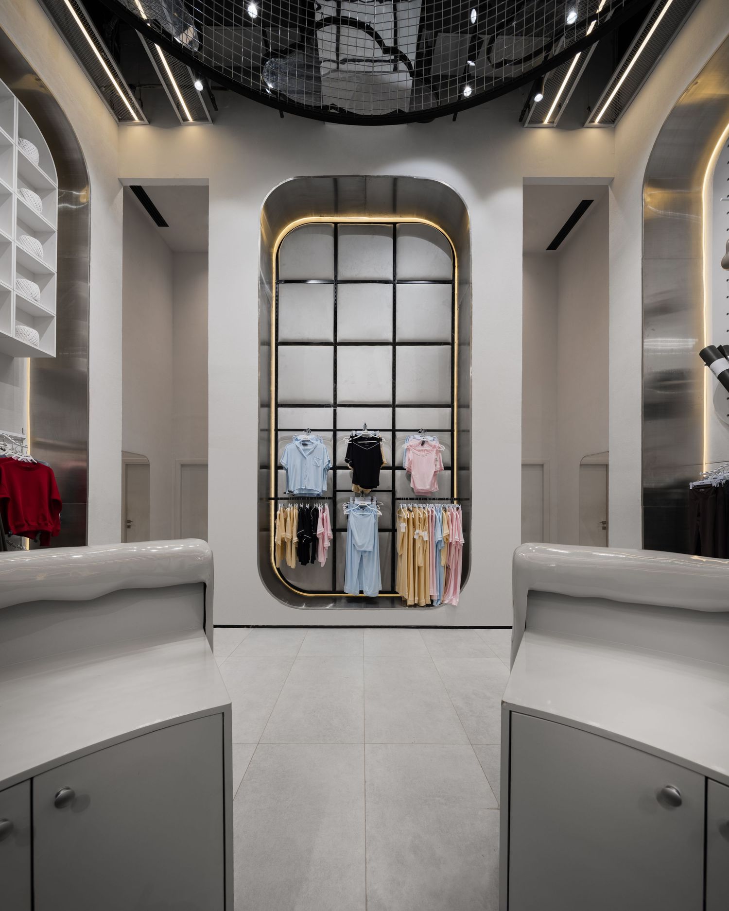 Modern clothing boutique interior with arched display niche, hanging garments, and sleek grey cabinetry.
