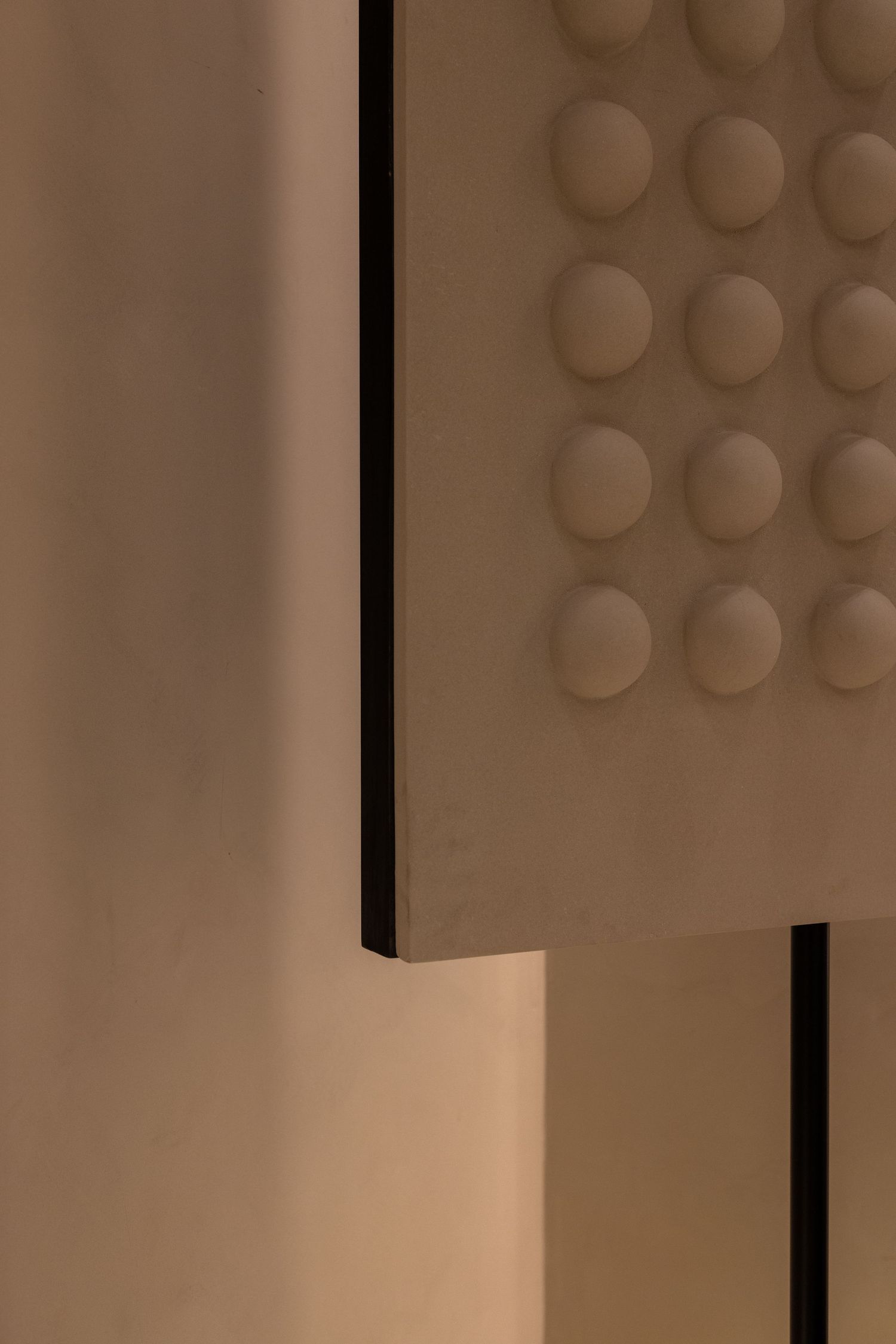 Close-up of textured beige panel with raised circular dot pattern against warm ambient lighting and dark frame edge.