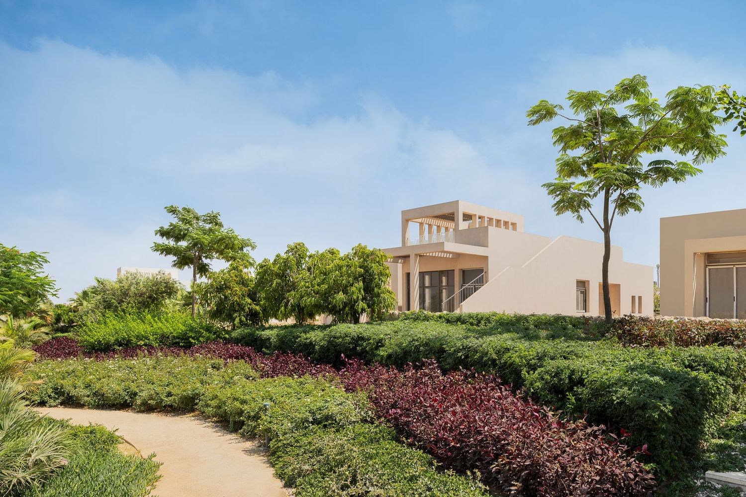 Luxurious villa exterior with desert-inspired architecture surrounded by manicured hedges and colorful garden paths.