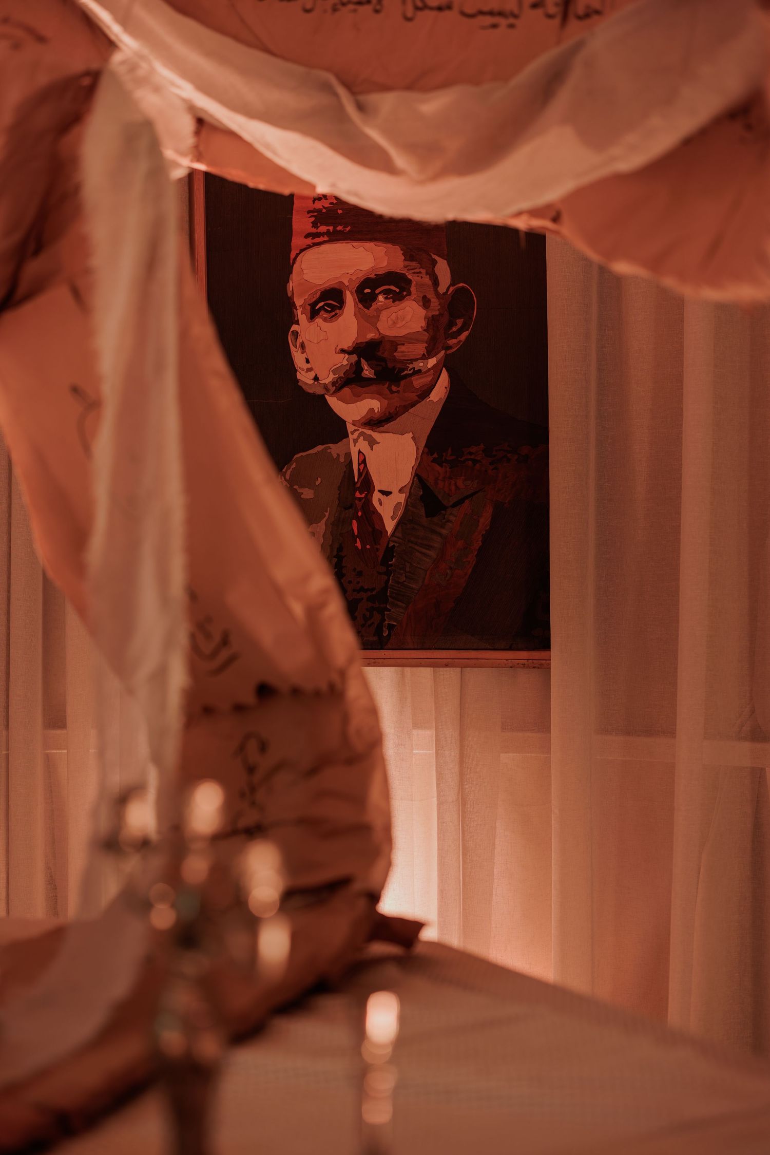 Portrait of mustachioed man in traditional Ottoman attire framed by draped peach fabric with Arabic text.