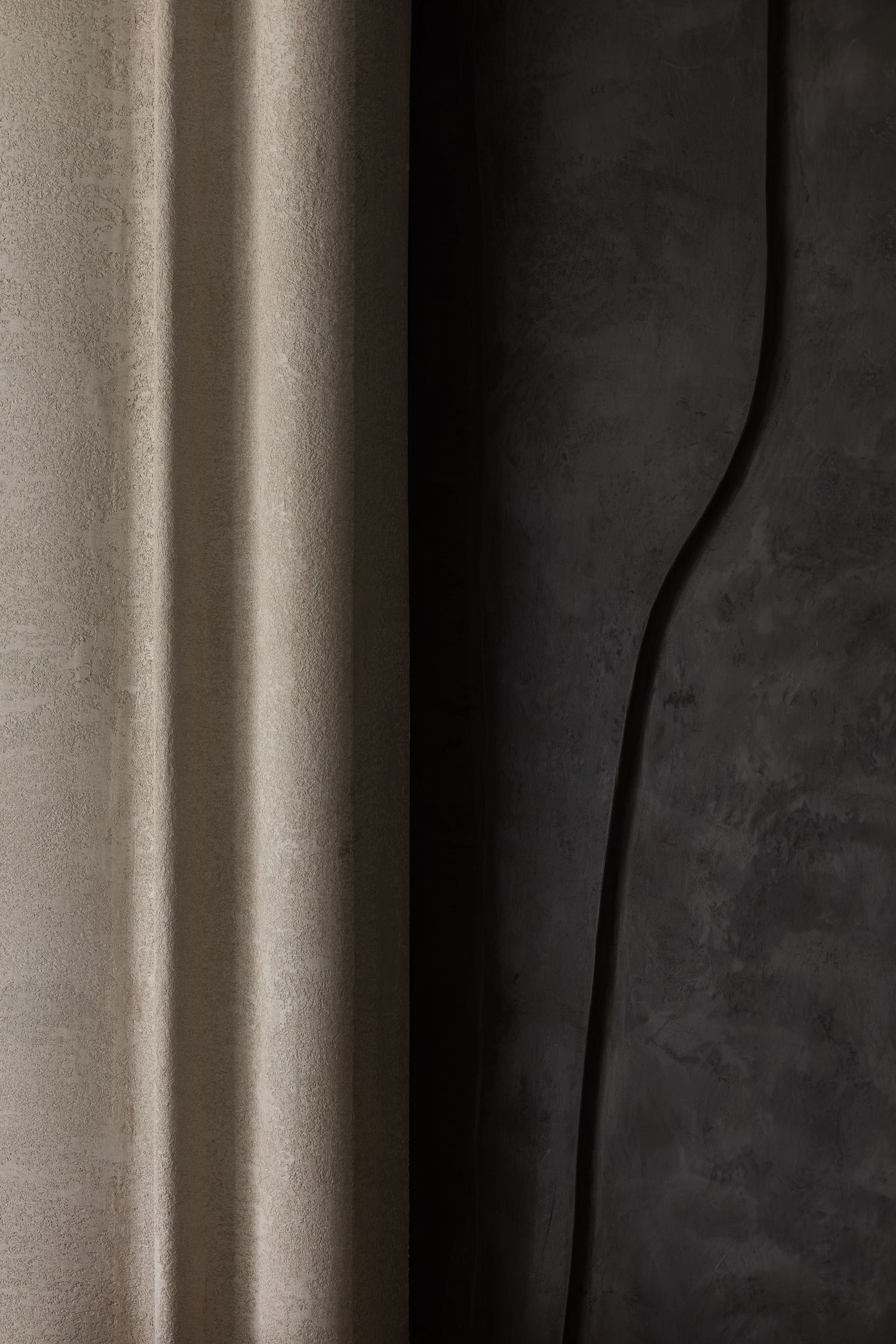 Contrasting beige velvet curtain panel beside dark textured concrete wall in a luxury interior.