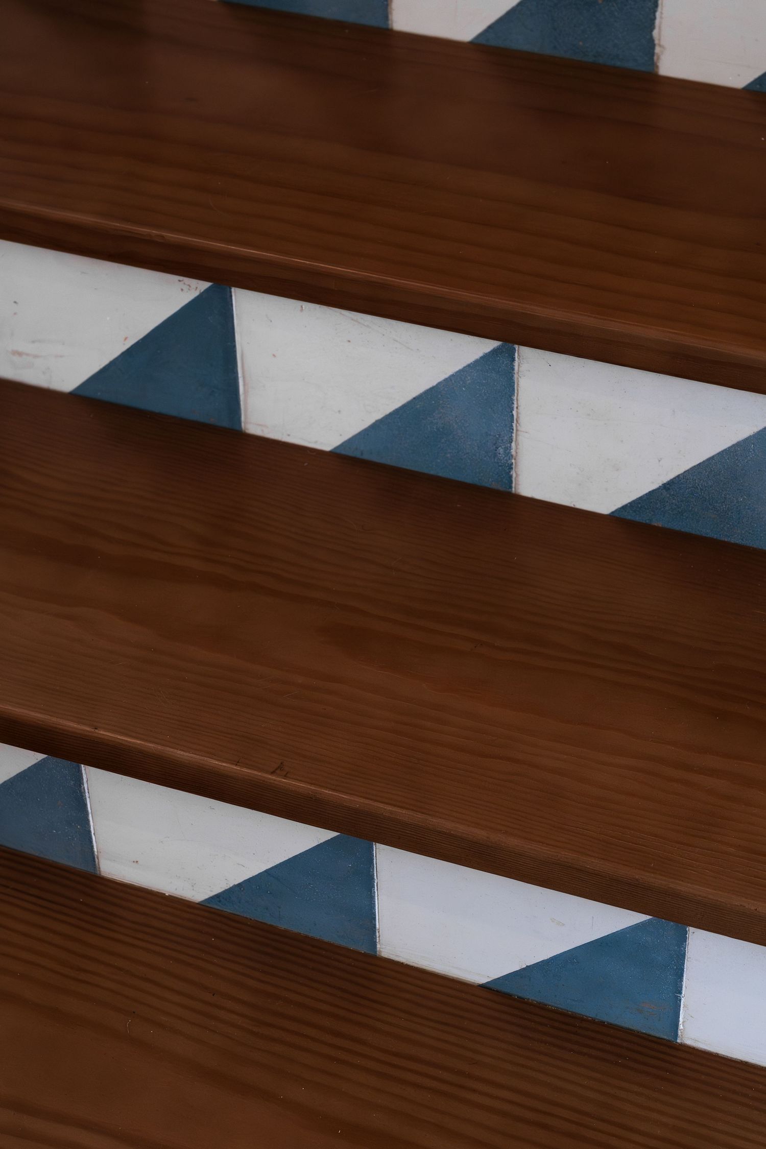Wooden stair treads with blue and white geometric triangle pattern tile risers in a modern staircase.