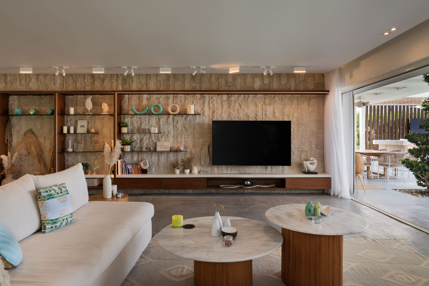 Contemporary living room with wooden feature wall, built-in shelving, flat-screen TV, cream sofa, and outdoor terrace access.