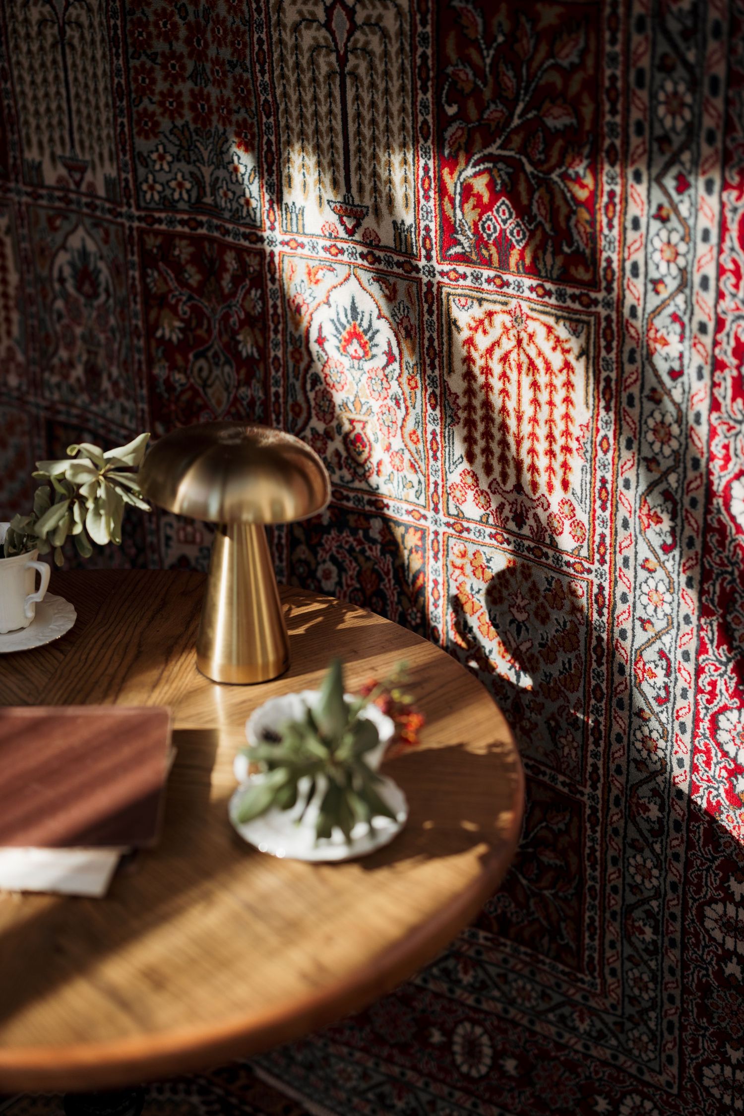 Golden mushroom table lamp on round wooden table with succulent, sunlight casting shadows on tapestry.
