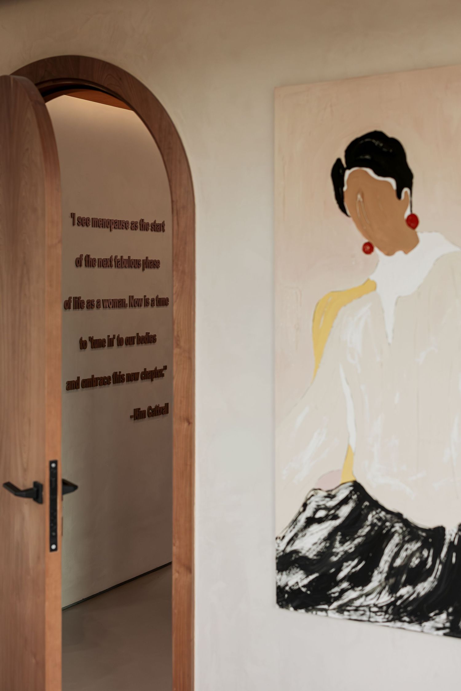 Arched wooden doorway with inspirational quote wall art beside a stylish portrait painting of a woman with red earrings.