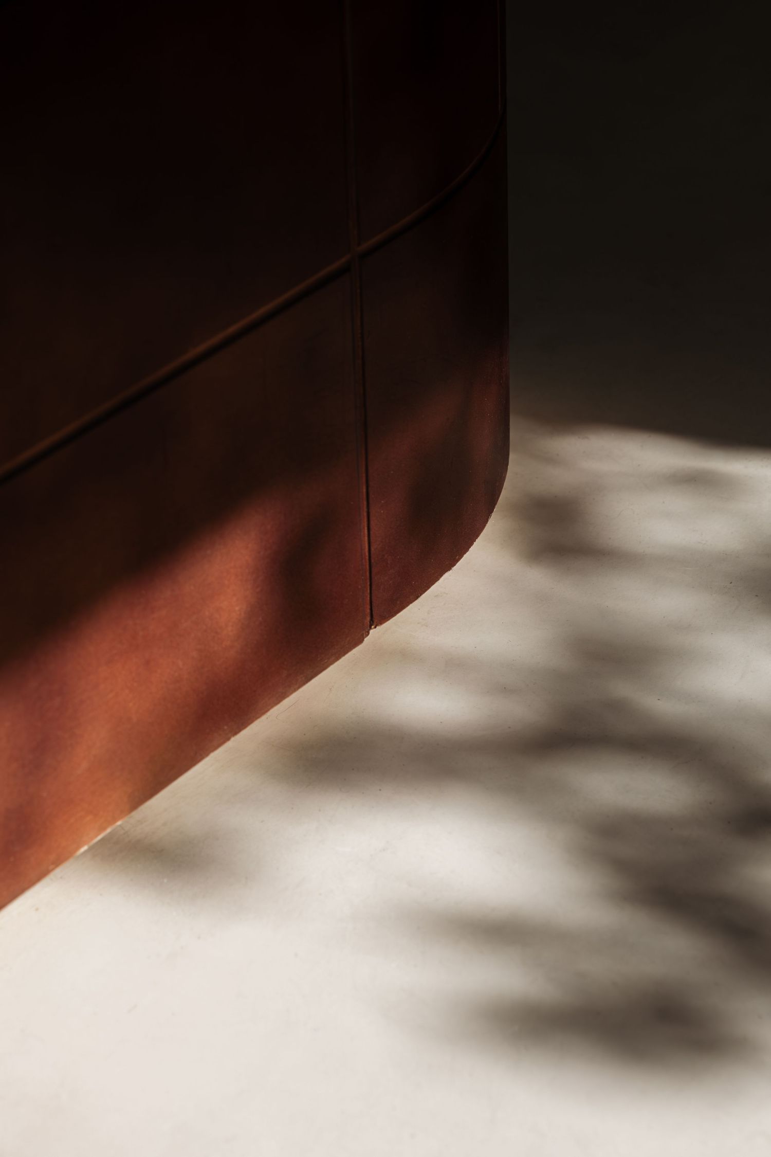 Close-up of a curved dark brown leather surface with dappled sunlight shadows on a concrete floor.