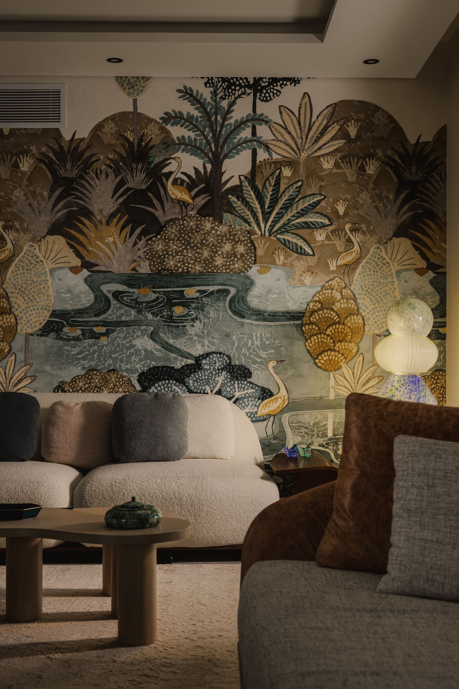 Luxurious living room featuring dramatic tropical botanical wallpaper mural, curved cream sofa, and round wooden coffee table.