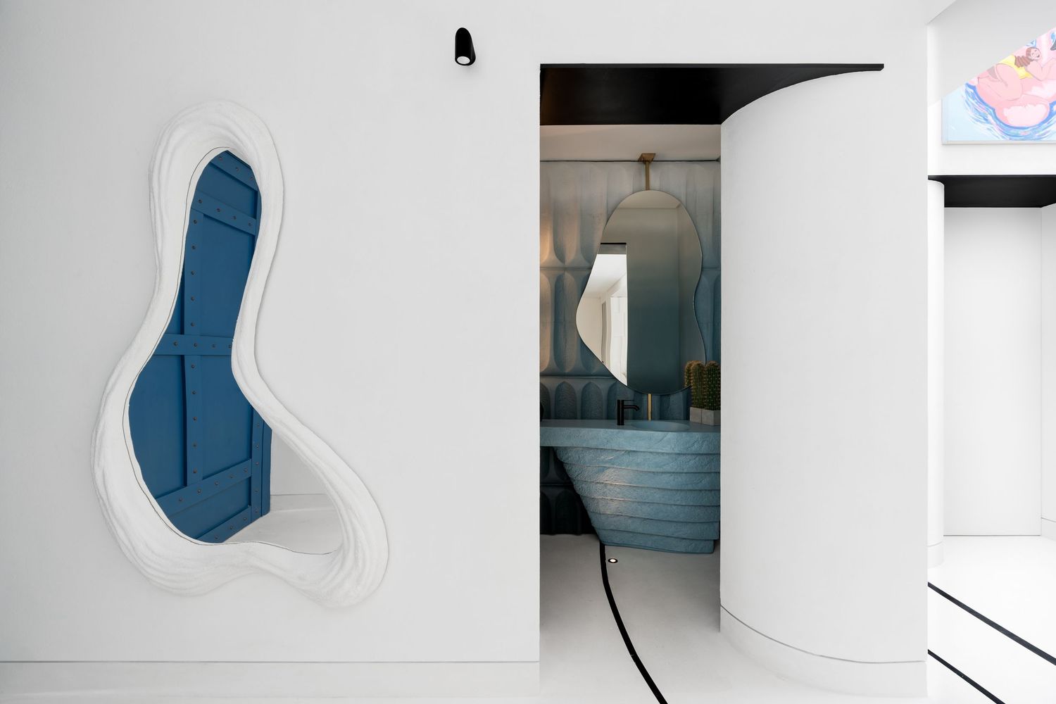 Modern white interior with organic blue mirror frame beside curved white column and blue bathroom.