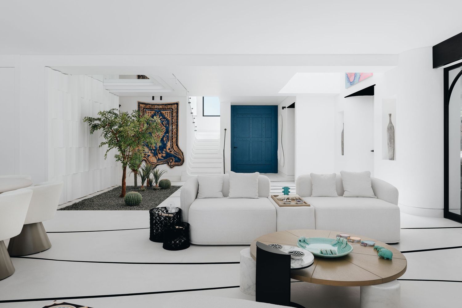 Modern white living room with sectional sofa, round wood coffee table, indoor plants, and blue accent wall decor.