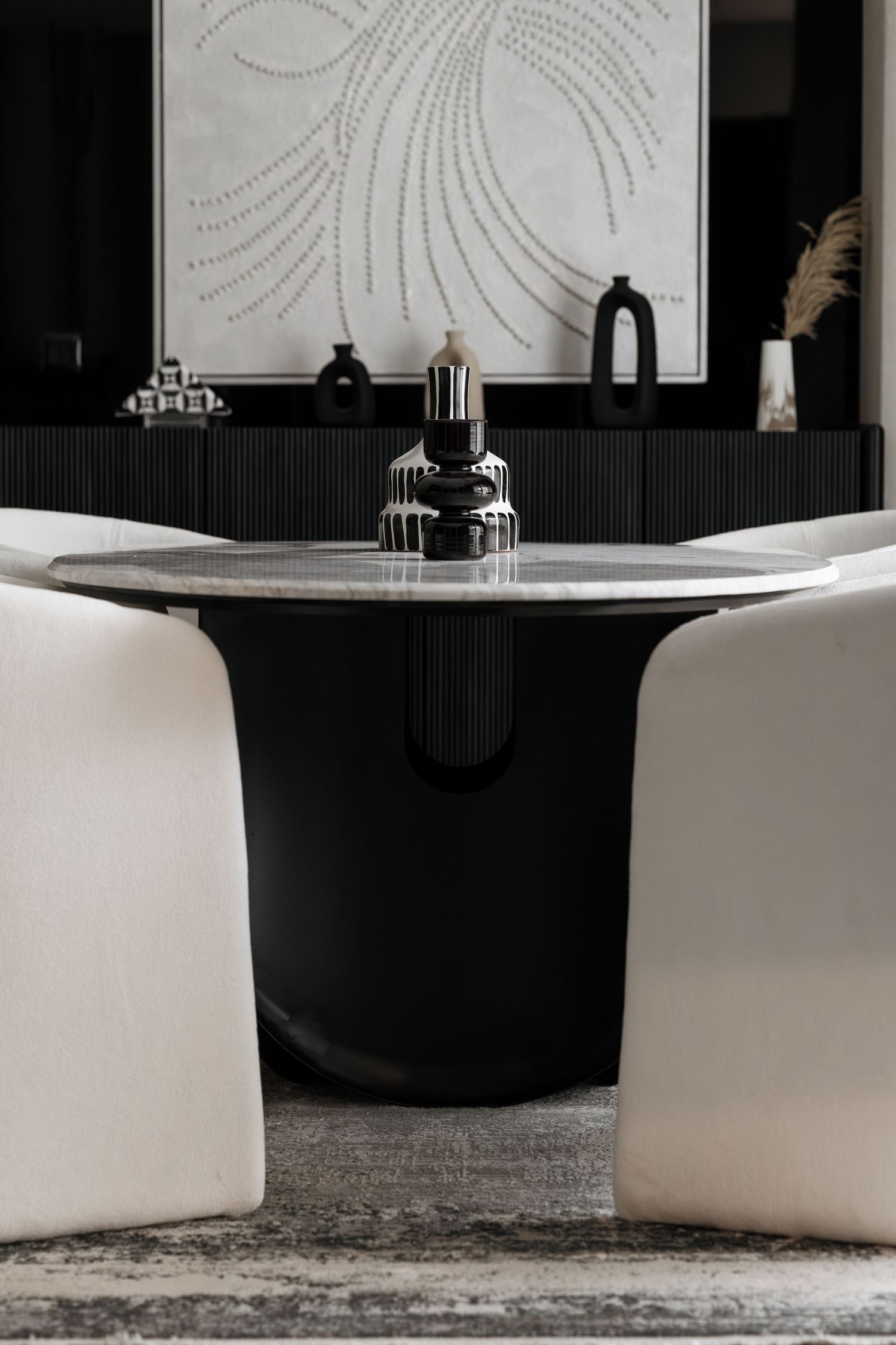 White curved dining chairs surrounding a black pedestal table with marble top in a modern dining room.