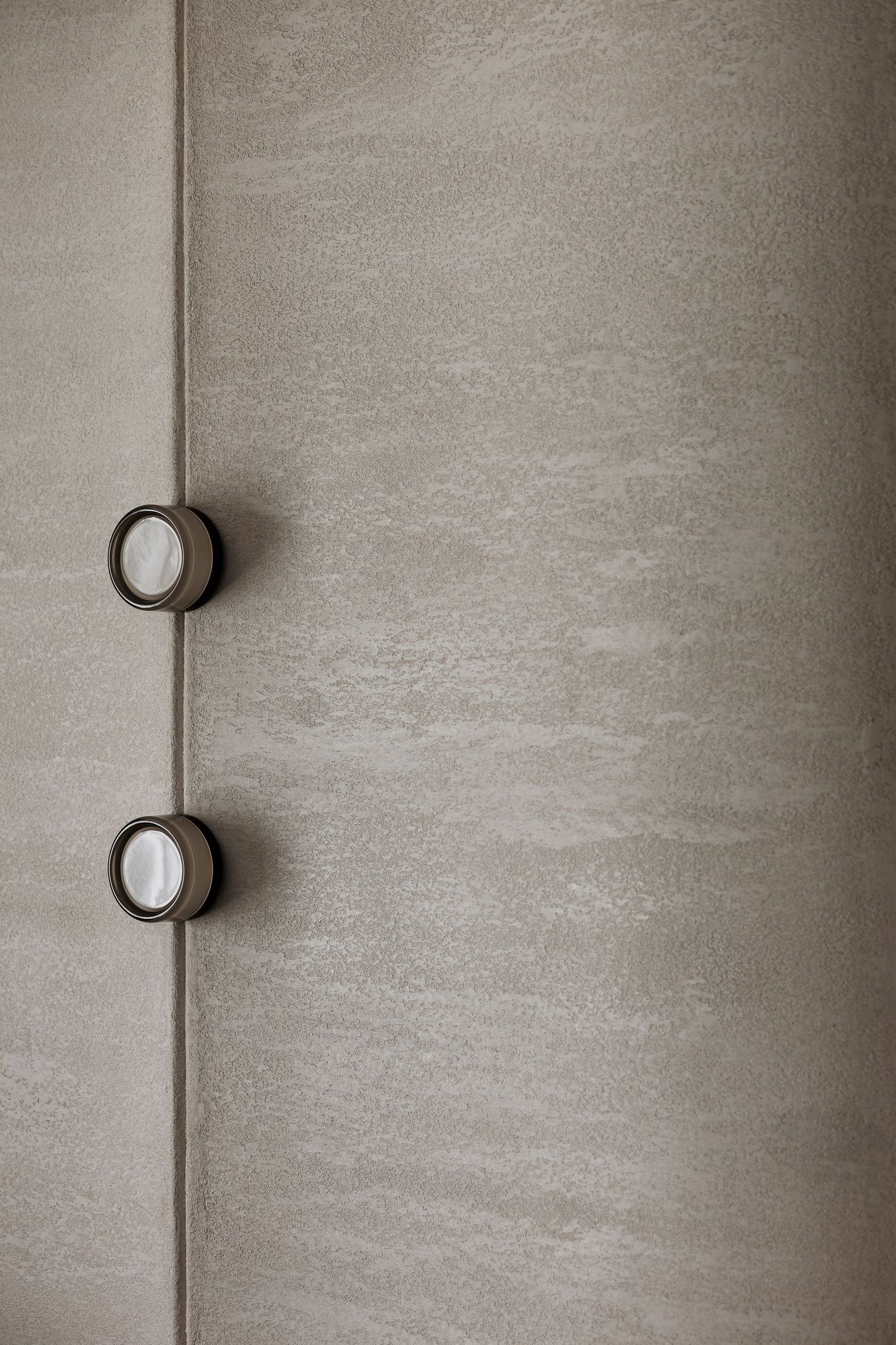Close-up of beige textured wall panel with two bronze circular wall sconces in a contemporary interior.