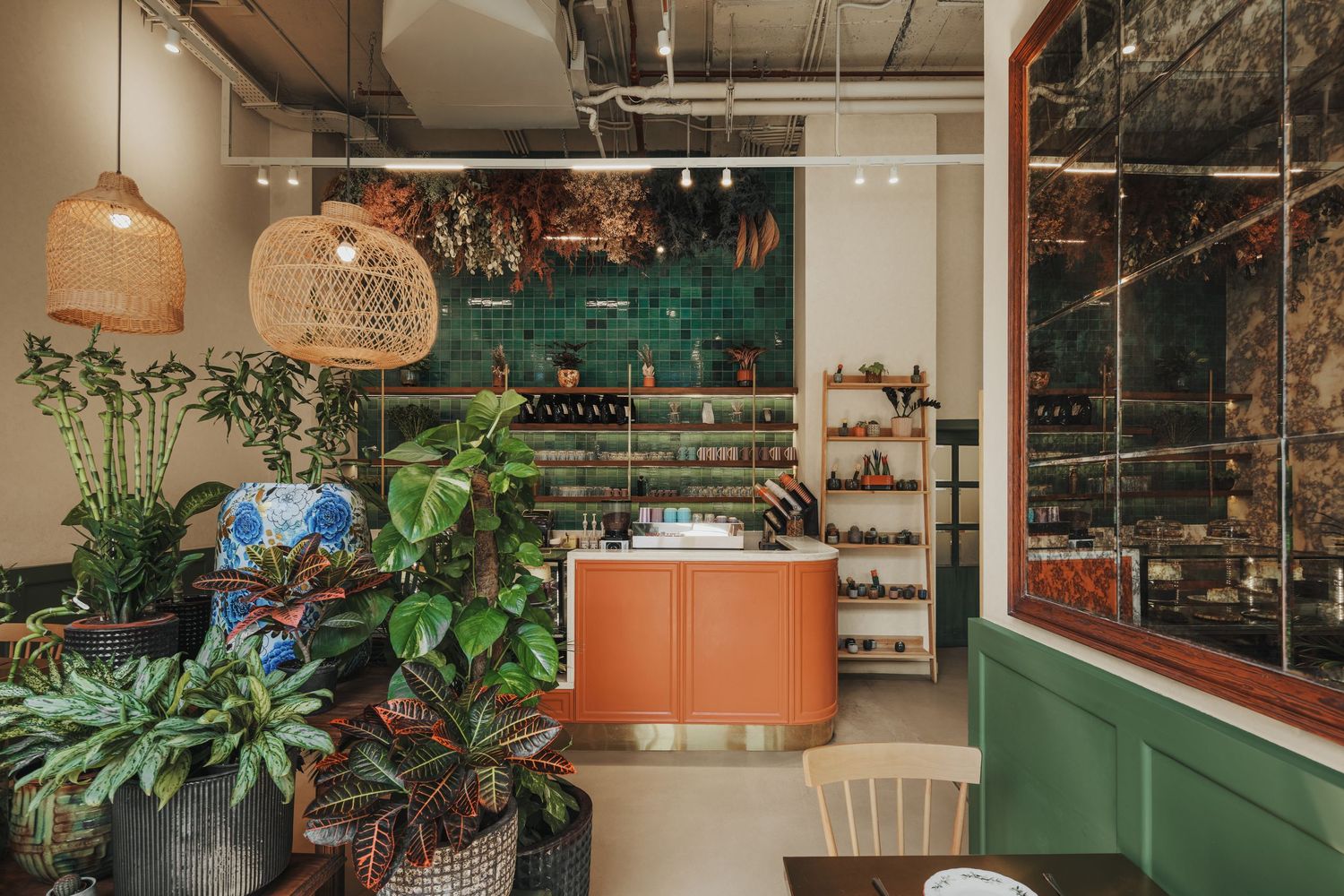 Vibrant cafe interior with lush plants, green tile backsplash, orange counter, and wall shelving.