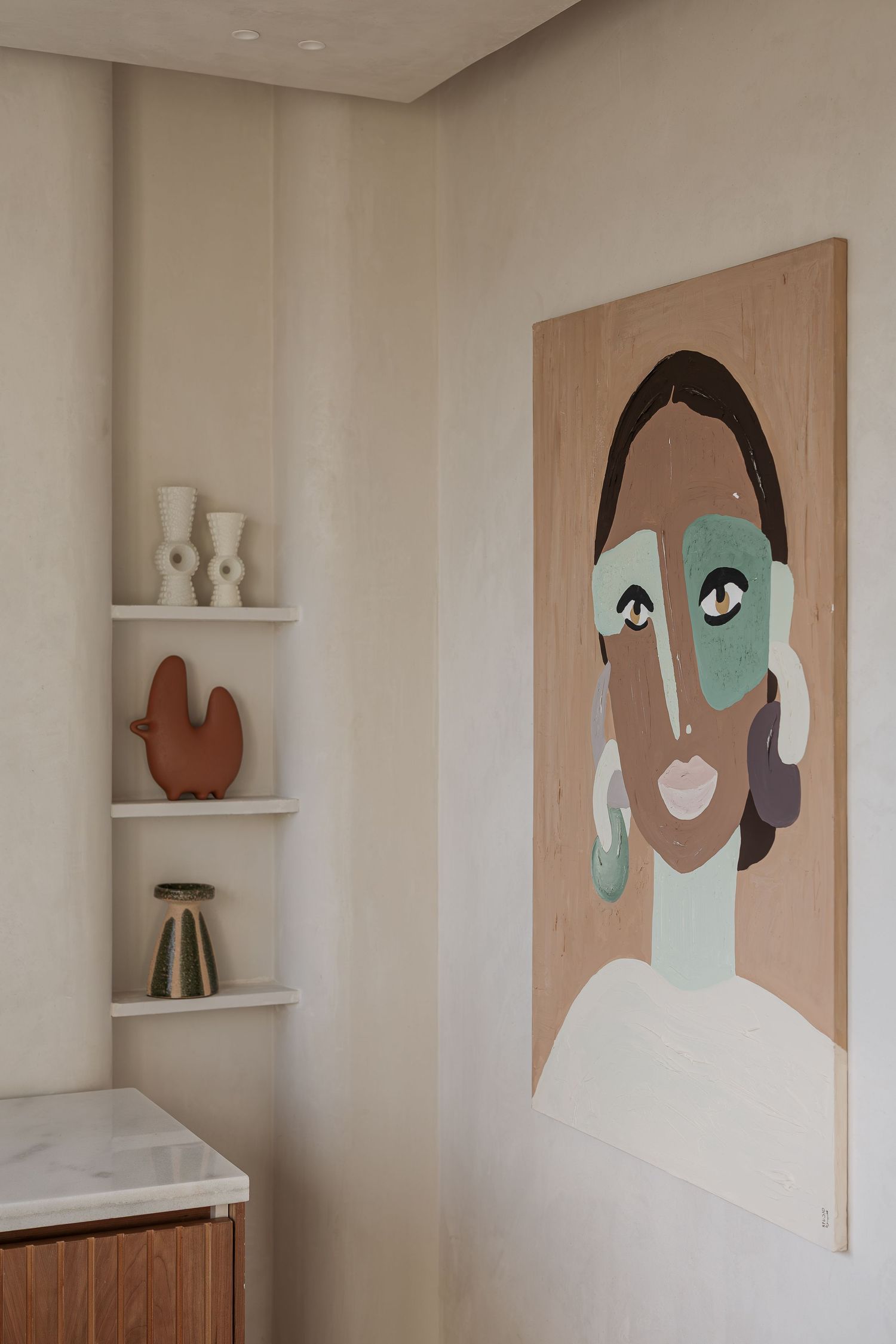 Minimalist beauty studio corner with abstract portrait artwork on wood panel and ceramic decorative vases on shelves.