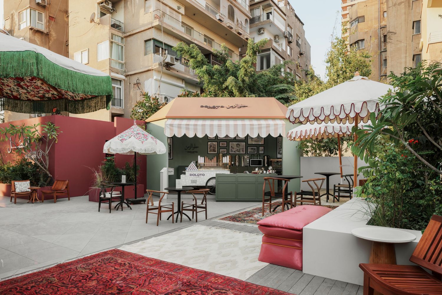 Charming outdoor cafe with striped awnings, vintage Persian rug, and lush greenery in urban courtyard.