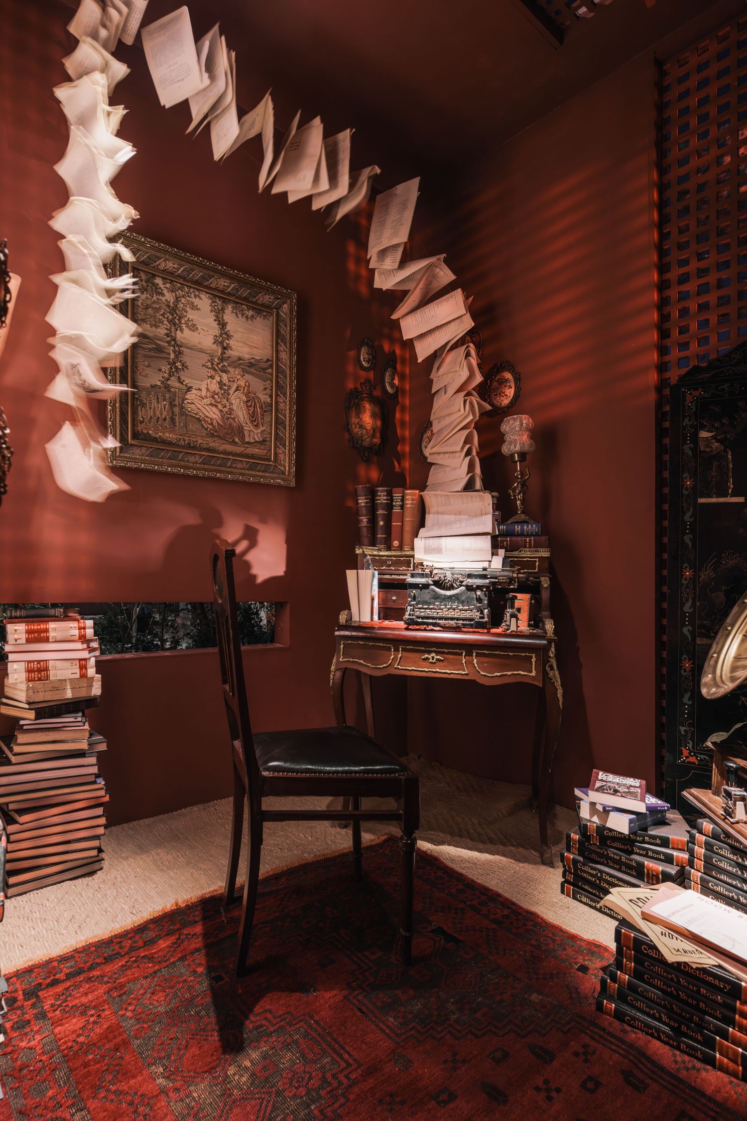 Artistic installation of flying books above a vintage typewriter desk in a dark red study room.