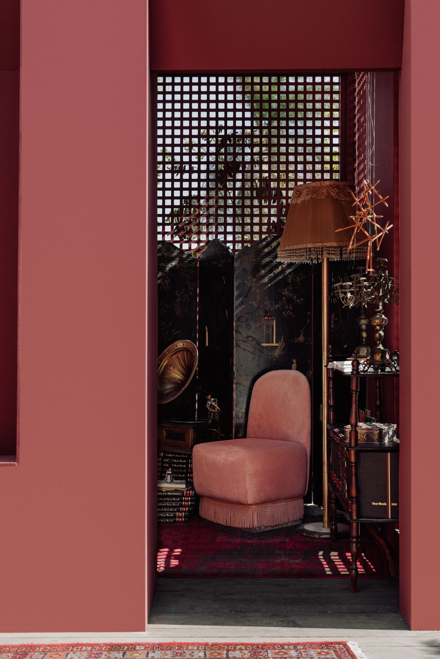 Elegant pink velvet chair in a rose-colored room with lattice screen, floor lamp, and antique decor.