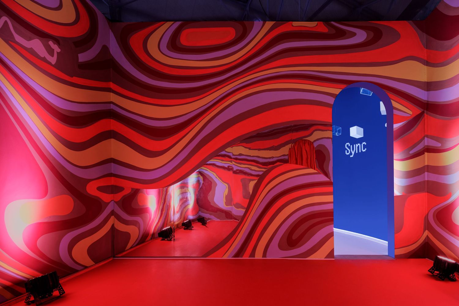 Colorful swirling red and purple wavy mural with a blue Sync kiosk in an immersive exhibition.
