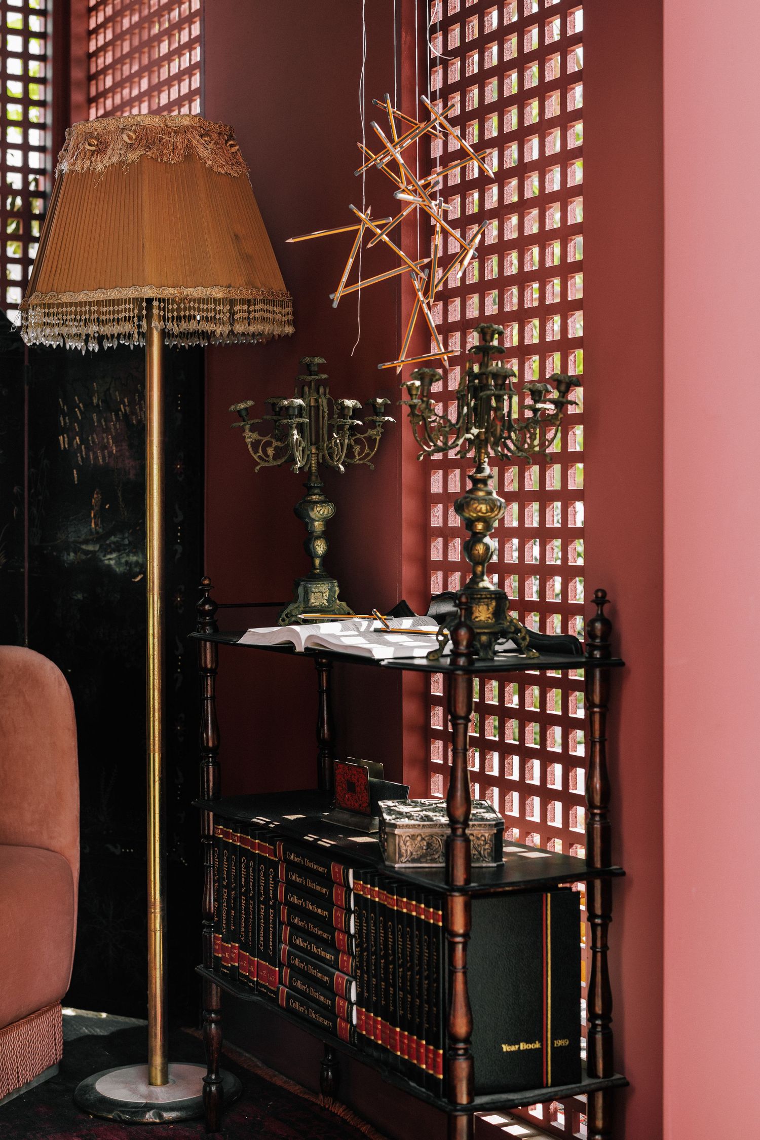 Vintage reading nook with fringed floor lamp, bookshelf, candelabra, and rose-colored lattice wall.